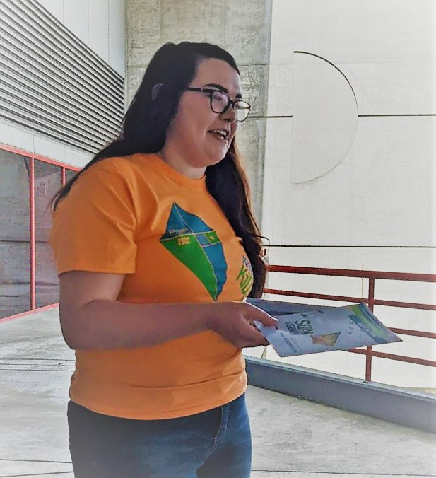 A person with long brown hair and orange Kites for Kids t-shirt holds kite-decorated pamphlets