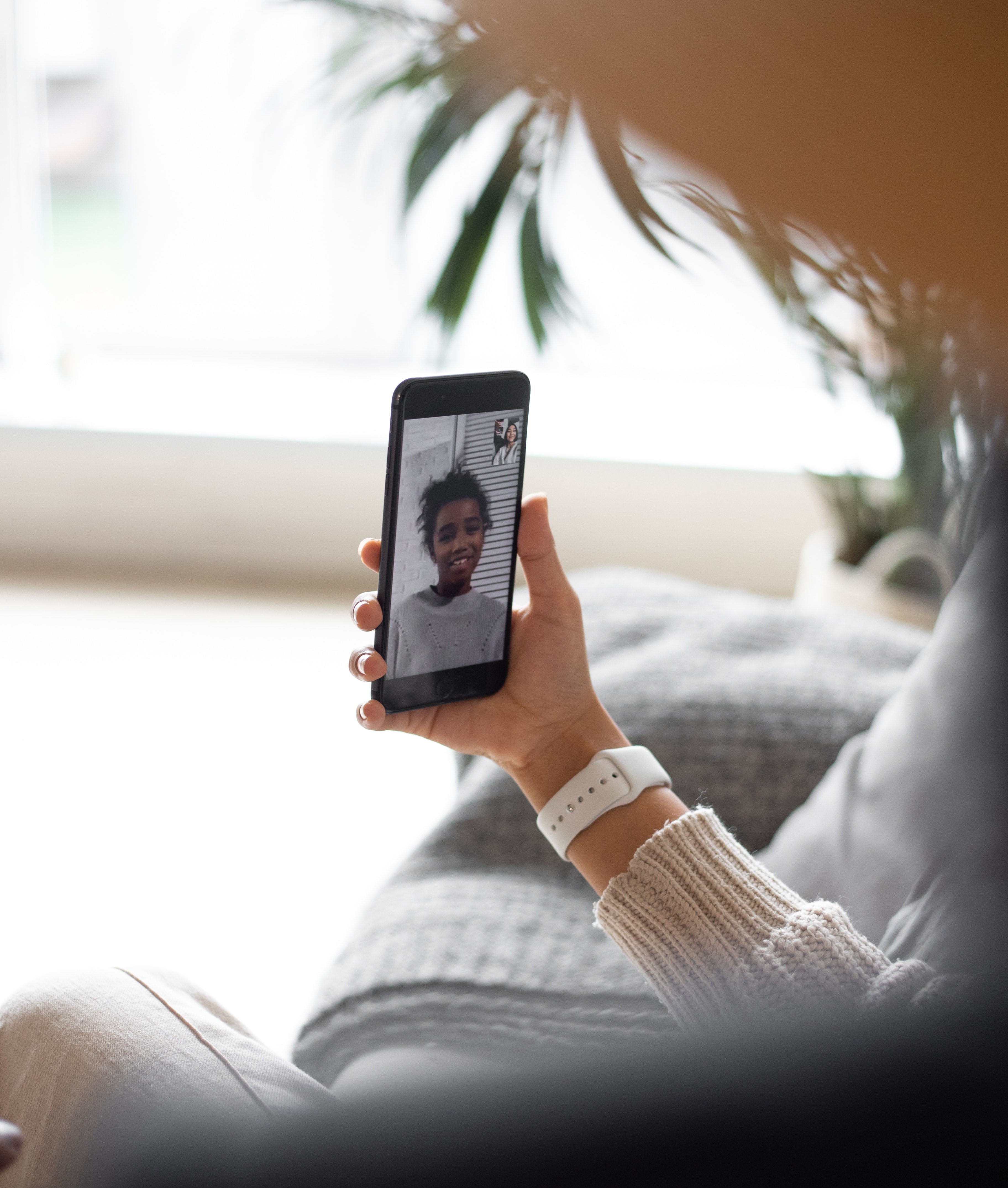 Two people on a video call: a hand holds up a cell phone, which shows the face of another person on the other end