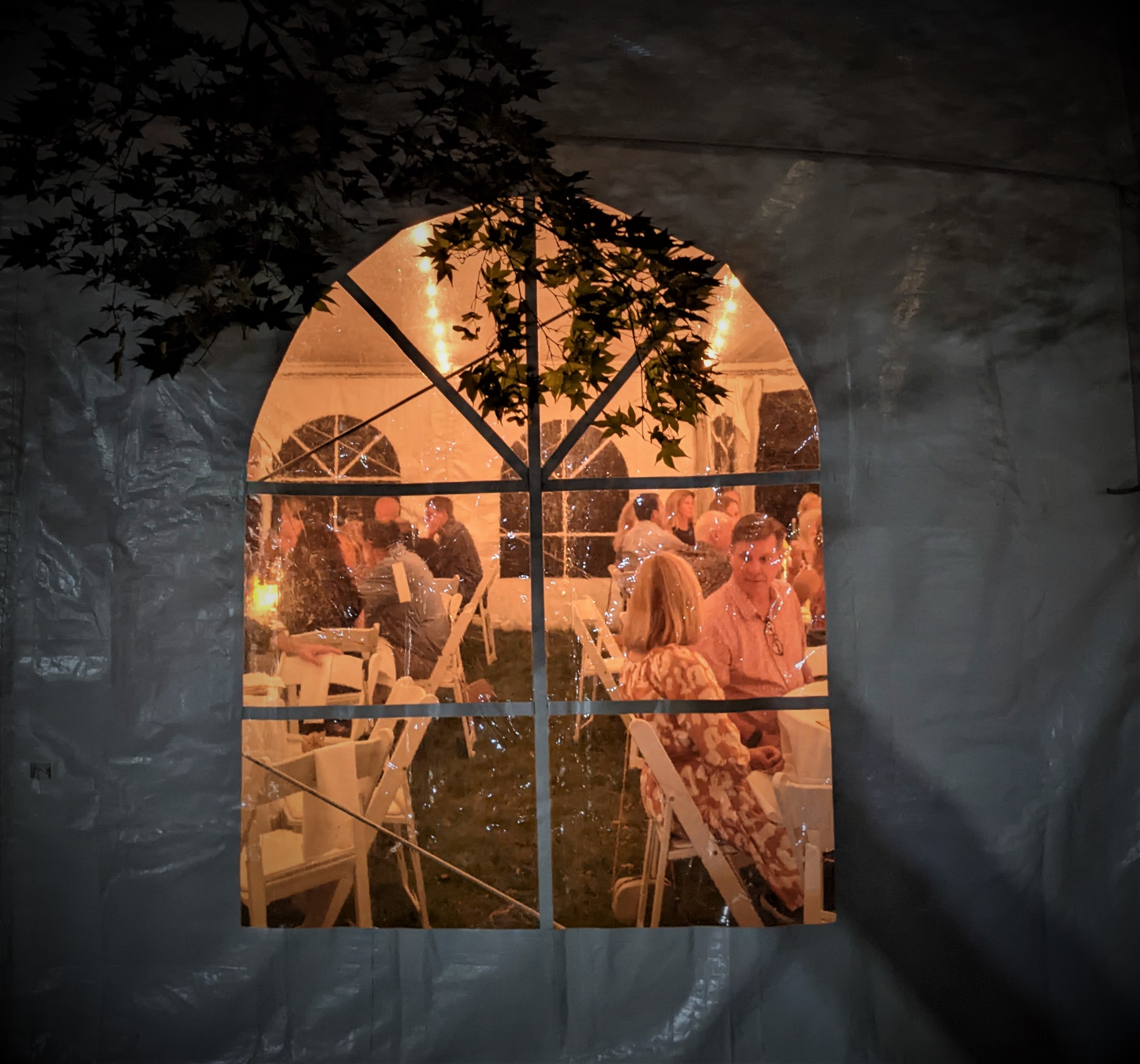 Photo through an orange-lit window in a tent shows guests talking and eating